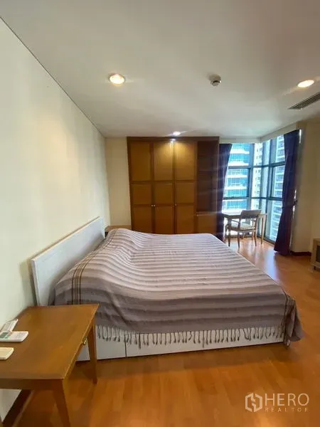 Condominium for rent in Pathum Wan, Bangkok - Spacious bedroom with large bed, built-in wooden wardrobe, and a small desk by a corner window.