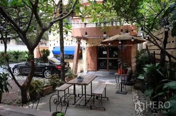 Detached House for rent in Watthana, Bangkok - Courtyard with picnic-style tables under string lights and trees, the house entrance and side parking area.