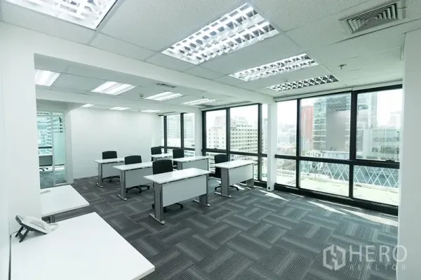 Office Space for rent - Workspace with multiple workstations, carpet tiles and wall-to-wall windows offering urban views.