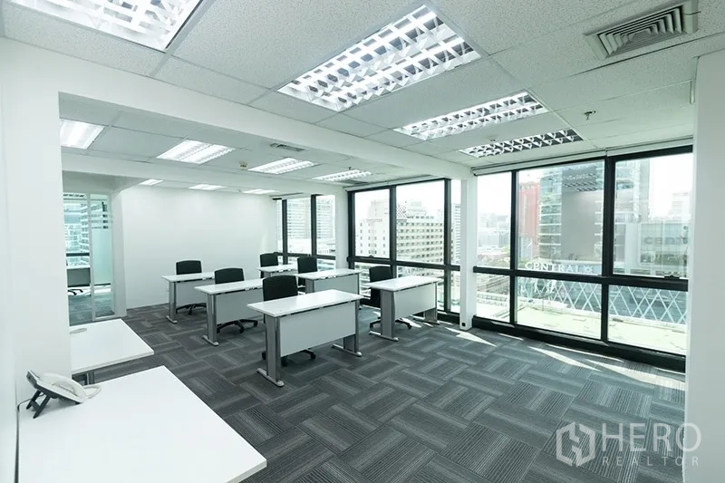 Office Space for rent - Workspace with multiple workstations, carpet tiles and wall-to-wall windows offering urban views.