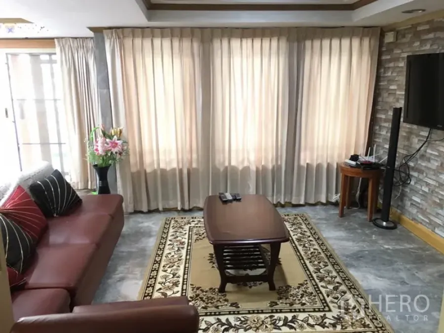 联排别墅 出租在Khlong Toei, Bangkok - 明亮客厅，皮沙发、落地窗帘、茶几及砖纹电视背景墙。