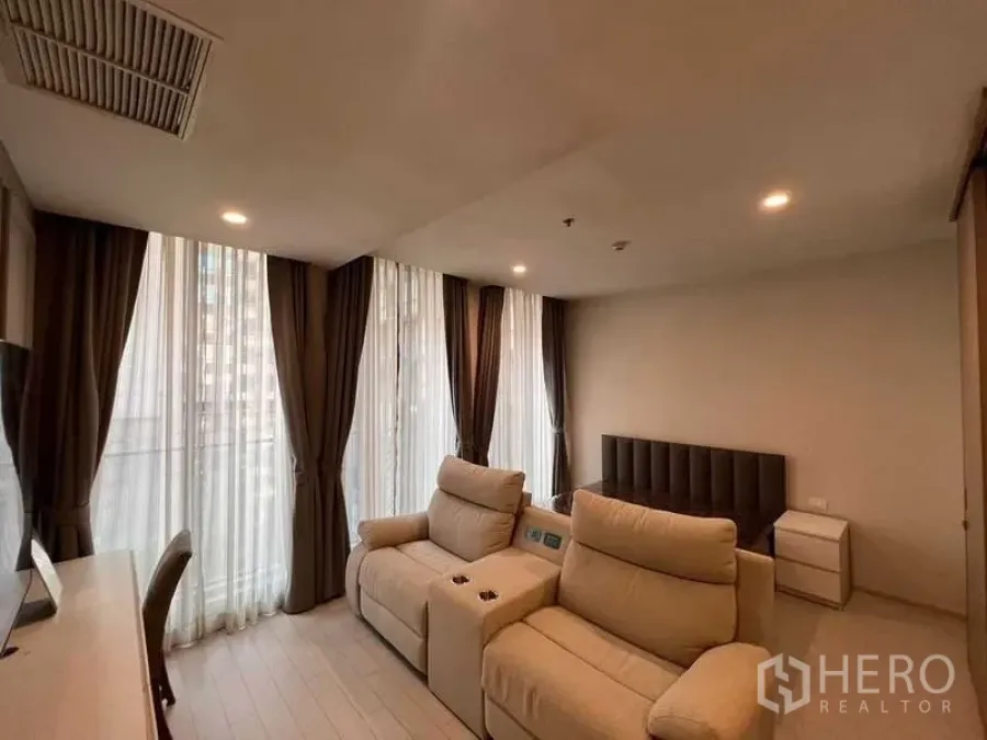 Condominium for rent in Pathum Wan, Bangkok - Wide view of open-plan living and sleeping zone with recliners, bed and wraparound windows.
