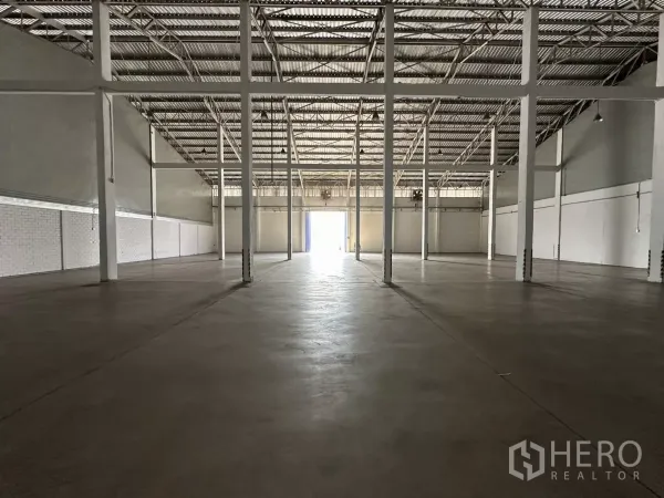 Warehouse for rent in Phra Khanong, Bangkok - Open warehouse interior with high steel truss roof, smooth concrete floor and rows of support columns.