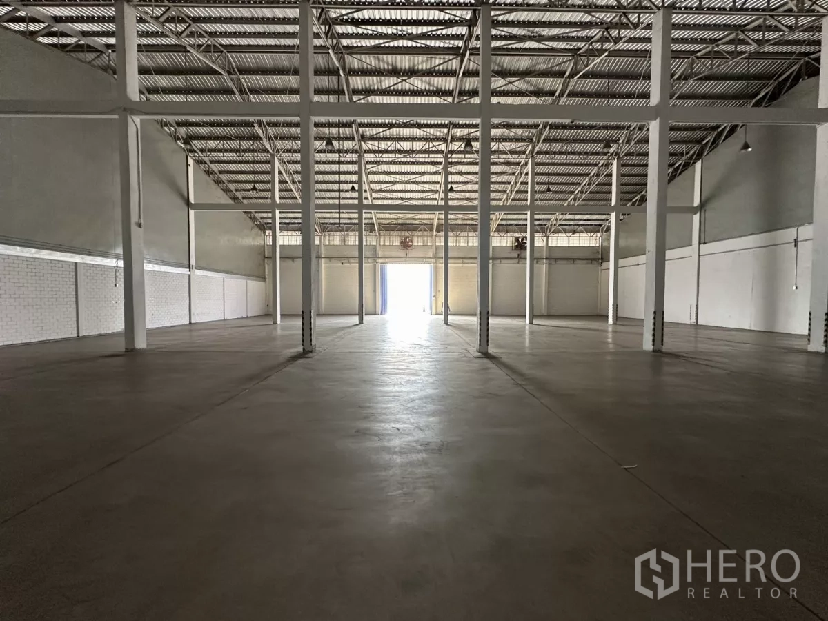 Warehouse for rent in Phra Khanong, Bangkok - Open warehouse interior with high steel truss roof, smooth concrete floor and rows of support columns.