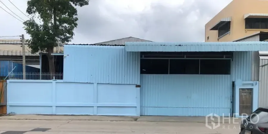 Warehouse for rent in Sai Noi, Nonthaburi - Street-facing light blue corrugated metal warehouse with gated wall and wide roller door.