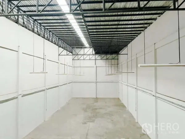 Factory for rent in Mueang Samut Sakhon, Samut Sakhon - Long production hall with white walls, suspended LED strip lights, and concrete floor under a metal roof.