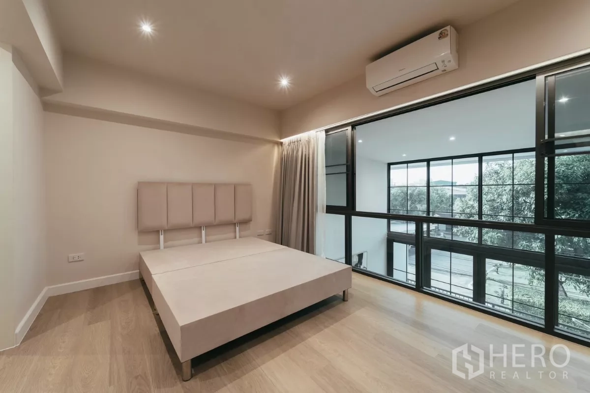 Townhouse for rent in Watthana, Bangkok - Bedroom overlooking double-height dining through black-framed windows, with air-conditioning.