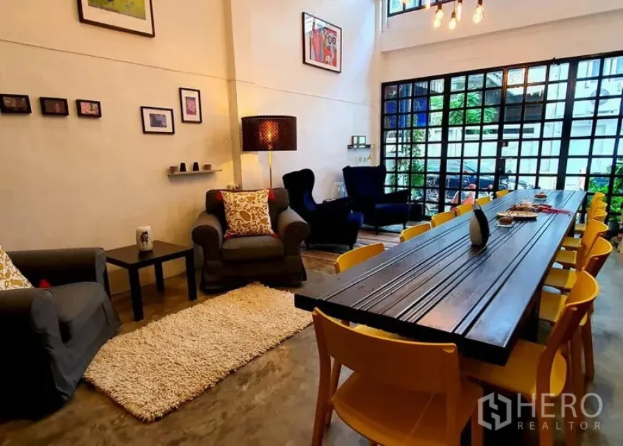 Townhouse for rent in Khlong Toei, Bangkok - Loft-style living and dining area with long table, yellow chairs, armchairs and black-framed glass doors.