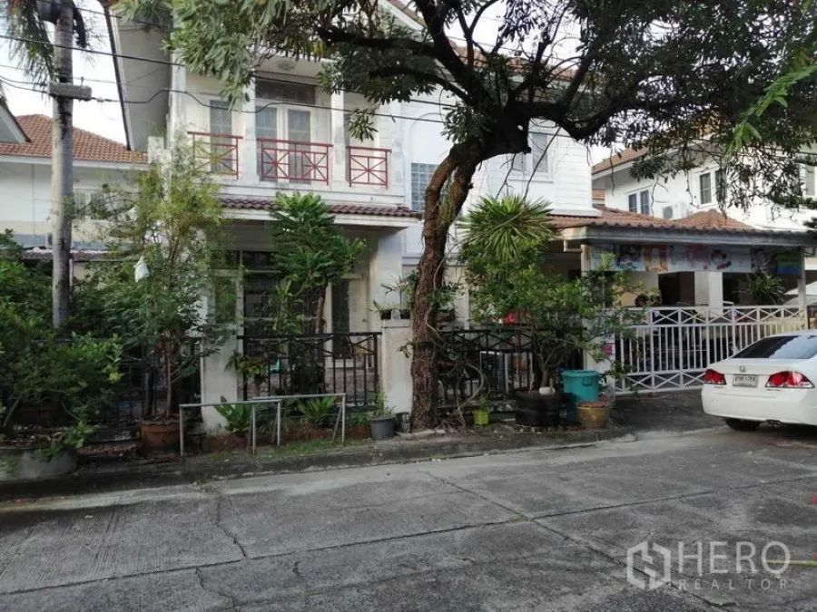 Detached House for sale in Prawet, Bangkok - Street view of two-story detached house with balcony, trees and front yard.