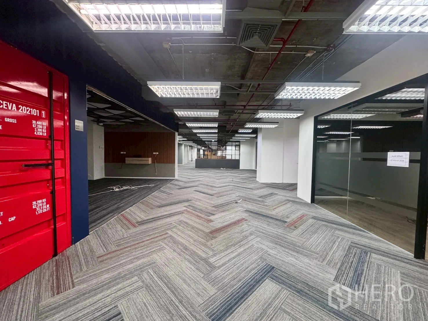 Office Space for rent in Watthana, Bangkok - Central aisle with a red container-style feature, glass rooms on the right, and grid lighting above.