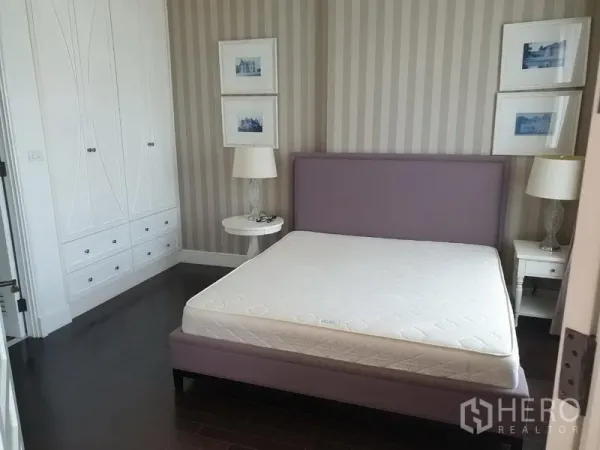 Condominium for rent in Khlong Toei, Bangkok - Cozy bedroom with upholstered bed, striped wallpaper and built-in white wardrobes.