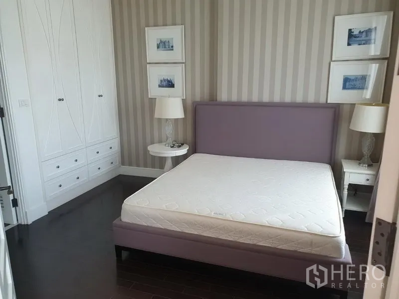 Condominium for rent in Khlong Toei, Bangkok - Cozy bedroom with upholstered bed, striped wallpaper and built-in white wardrobes.