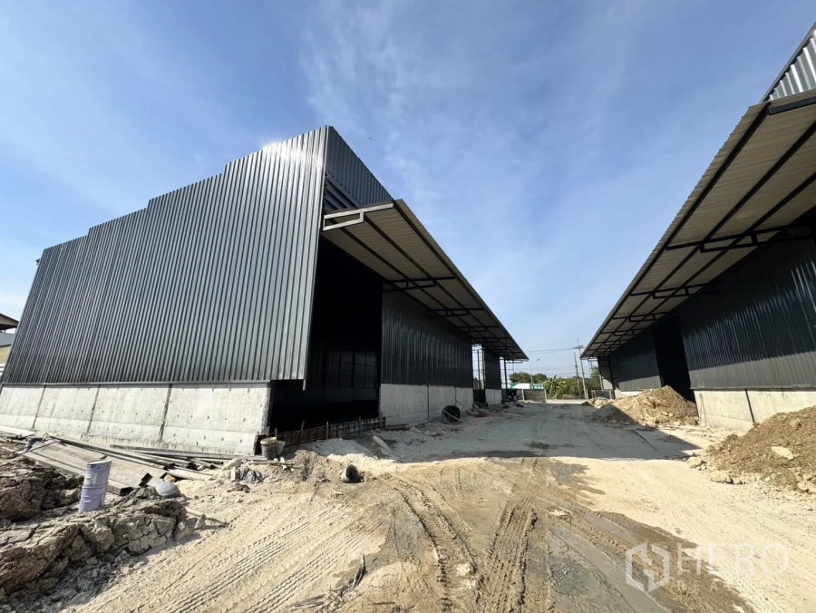 Warehouse for rent in Lam Luk Ka, Pathum Thani - Corrugated metal warehouse buildings with elevated concrete bases and a long loading lane.