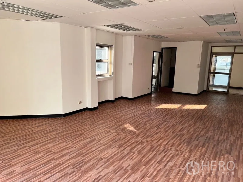 Office Space for rent in Pathum Wan, Bangkok - Corner workspace featuring windows, overhead fluorescent panels, and a doorway to internal facilities.