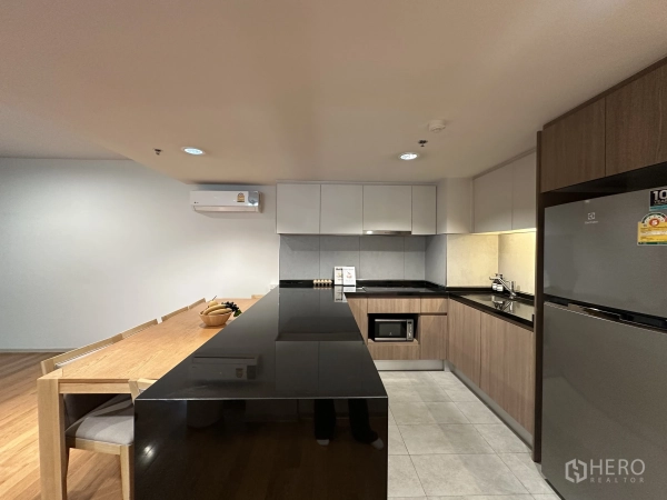 Condominium for rent in Khlong Toei, Bangkok - Contemporary kitchen with long black island, built-in cabinets, and dining table.