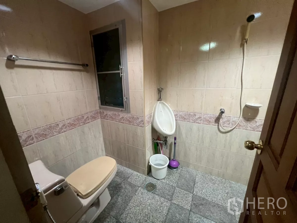 Shophouse for rent in Bang Rak, Bangkok - Tiled bathroom with toilet, urinal, handheld shower and small window.
