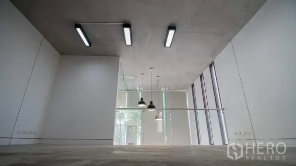 Townhouse for rent or sale in Phra Khanong, Bangkok - Loft-style area with exposed concrete ceiling, pendant lights and a glass partition.