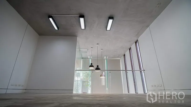 Townhouse for rent or sale in Phra Khanong, Bangkok - Loft-style area with exposed concrete ceiling, pendant lights and a glass partition.