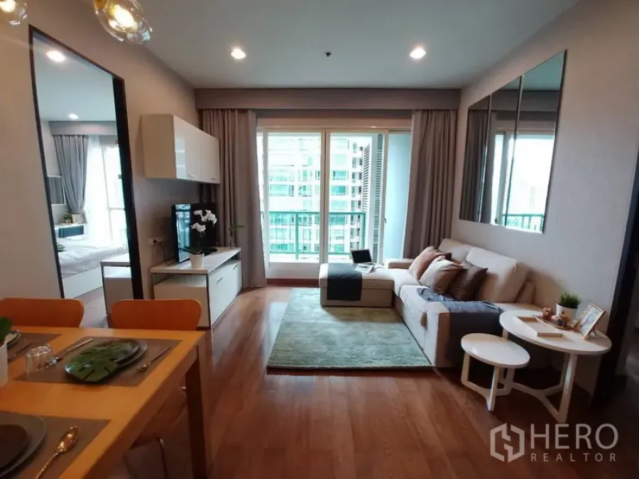 Condominium for rent in Pathum Wan, Bangkok - Bright living room with sofa, TV console, wood flooring and full-height balcony doors overlooking the city.