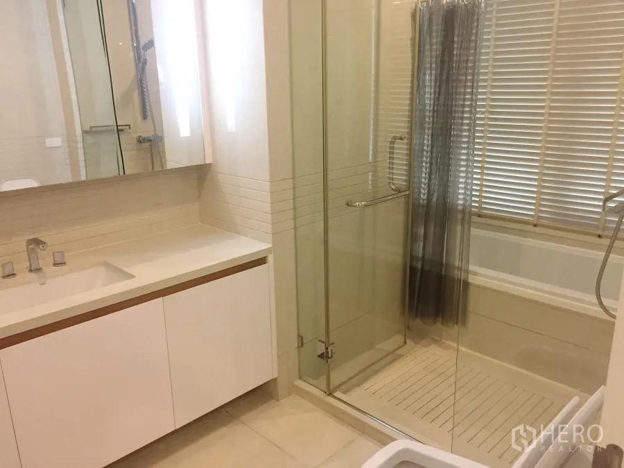 Condominium for rent in Pathum Wan, Bangkok - Modern bathroom with glass shower, bathtub, wide vanity and window blinds.