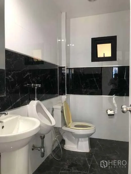 Factory for rent or sale in Samut Prakan - Clean restroom with toilet, urinal, sink and black-and-white wall tiles.