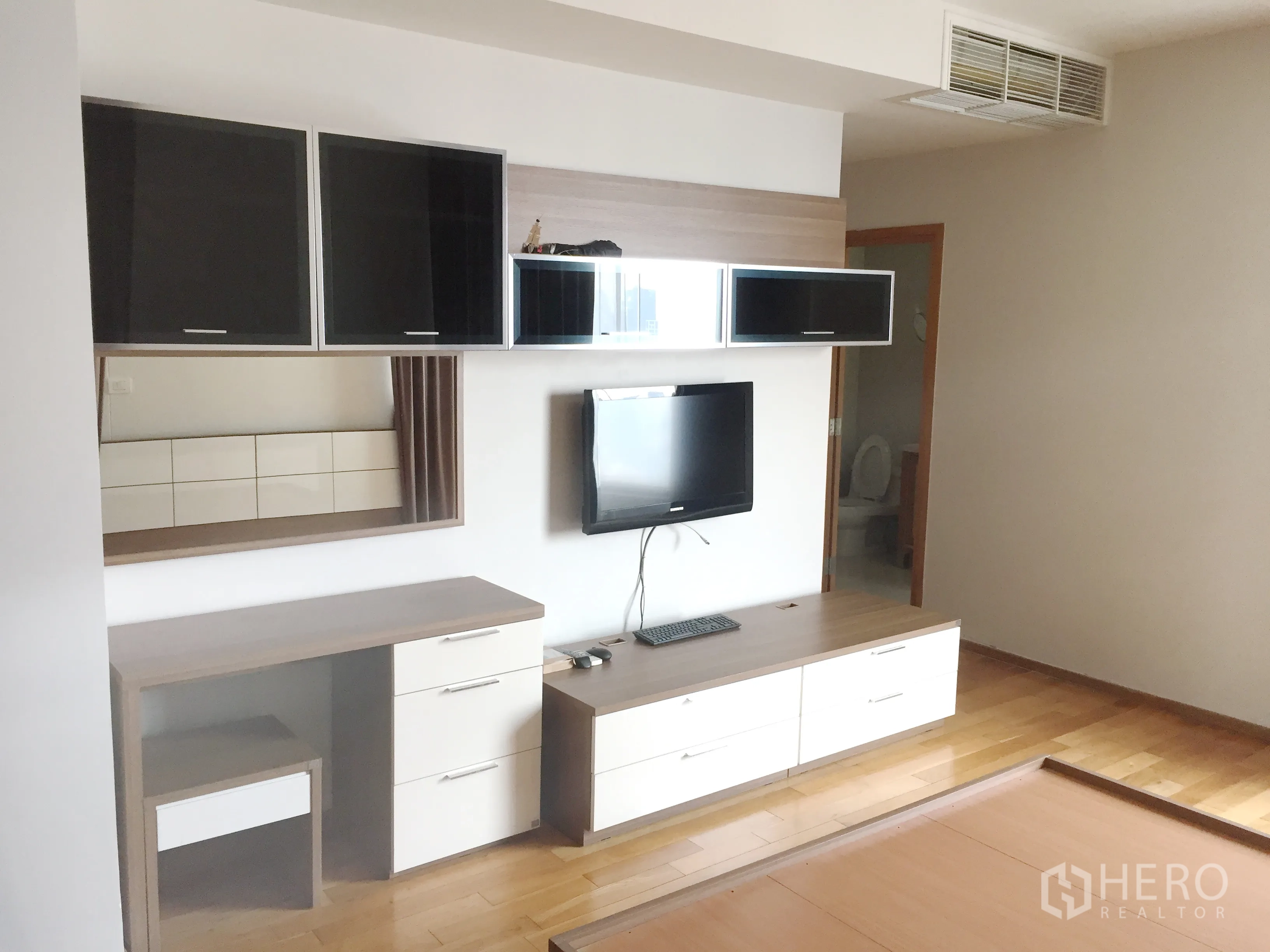 Condominium for rent in Khlong Toei, Bangkok - Bedroom media wall with mounted TV, storage drawers, and doorway to an en-suite bathroom.