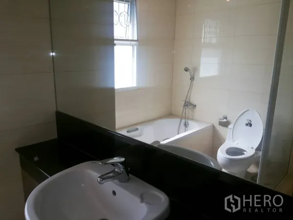 Apartment for rent in Khlong Toei, Bangkok - Bright bathroom with bathtub, handheld shower, toilet, and a vanity with large mirror.
