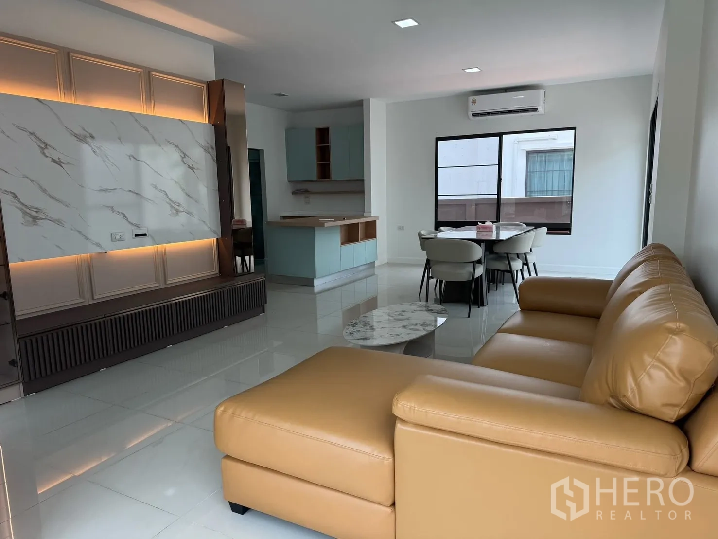 Detached House for rent in Prawet, Bangkok - Open-plan living and dining area with tan sofa, TV feature wall and dining set.