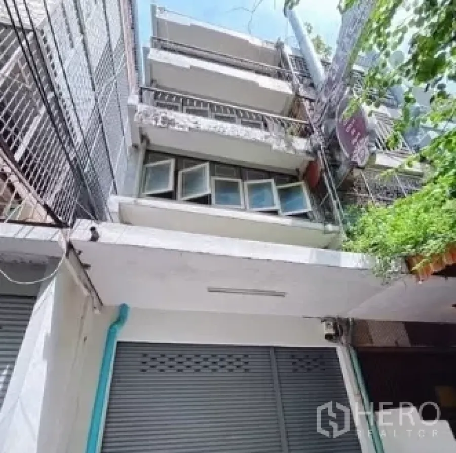 Shophouse for rent in Bang Rak, Bangkok - Four-storey shophouse facade with metal shutter and balconies in a Silom lane.