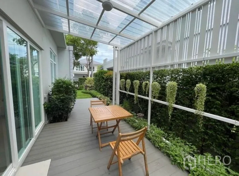 Detached House for rent in Prawet, Bangkok - Covered terrace overlooking a landscaped garden with hedge and outdoor table set.