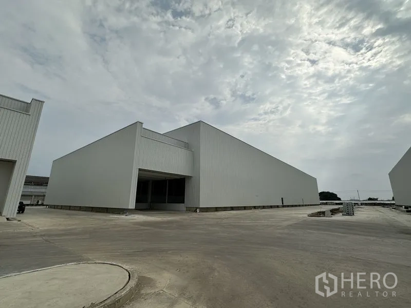 工厂 出租在Pathum Thani - 新建金属外墙厂房与宽阔硬化场地，阴天。
