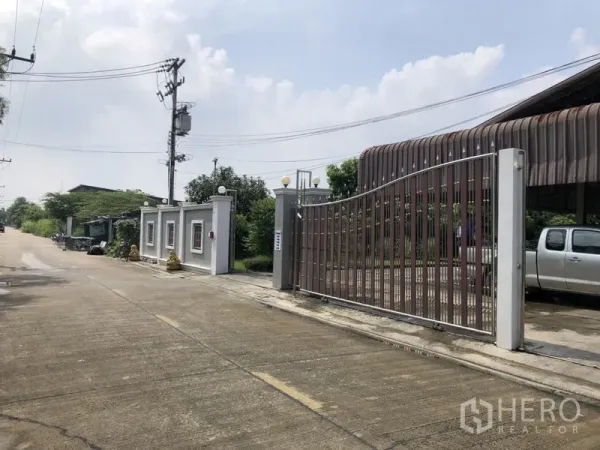 Detached House for sale in Lam Luk Ka, Pathum Thani - Close-up of the wide metal gate and boundary wall beside a paved street.