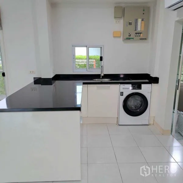 Detached House for rent in Prawet, Bangkok - Modern white kitchen with black stone countertops, sink and front-load washer.
