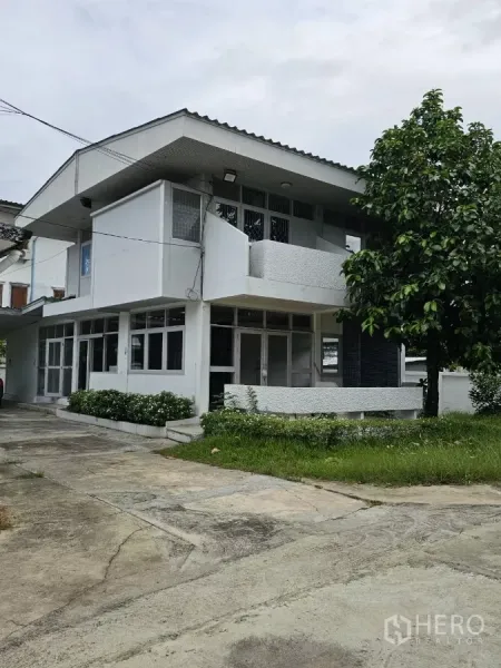 Detached House for rent or sale in Lat Phrao, Bangkok - Corner angle showing balcony, glazed doors, and grass beside the driveway.