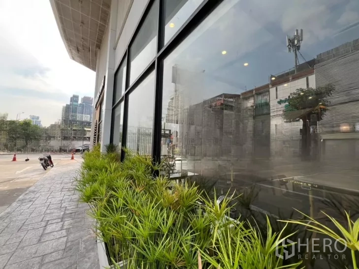 零售空间 出租在Watthana, Bangkok - 临街外立面，落地玻璃与绿植花槽，城市景观可见。