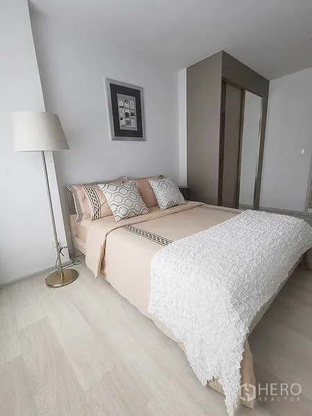 Condominium for rent in Pathum Wan, Bangkok - Second bedroom with beige bedding, floor lamp and closet.