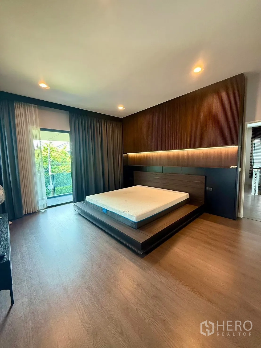 Detached House for rent in Bang Kapi, Bangkok - Master bedroom with platform bed, feature wall and garden-view windows.