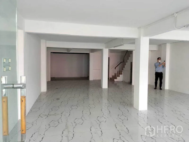 Shophouse for rent in Khlong Toei, Bangkok - Ground-floor retail area with white walls, marble-look tiles, columns and a glass entry.
