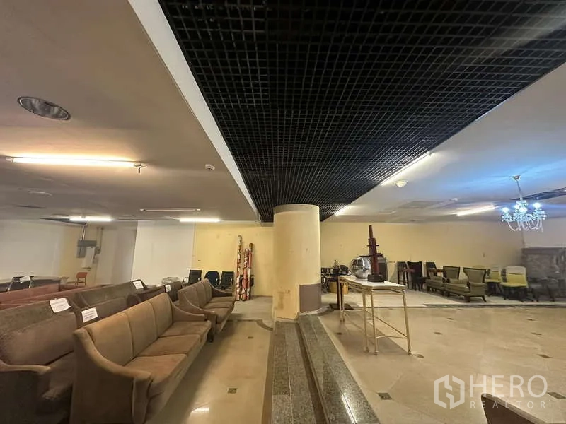 Retail Space for rent - Spacious shop floor with grid ceiling, central pillar, chandelier and tiled flooring.