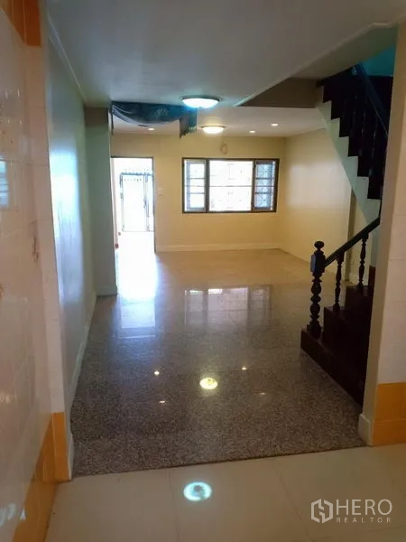Townhouse for rent in Phra Khanong, Bangkok - Bright living-dining space with front windows and a dark wood staircase.