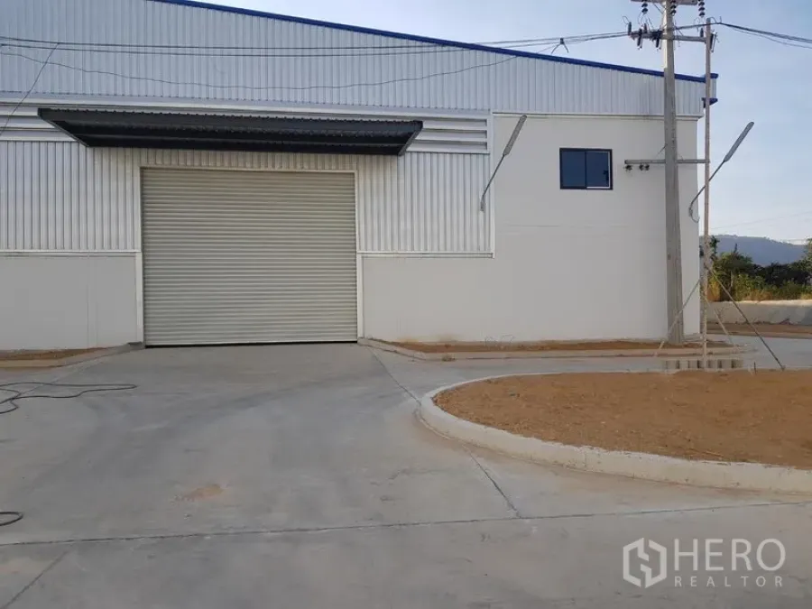 Factory for rent in Chon Buri - Modern factory exterior with large roller shutter door and concrete driveway.
