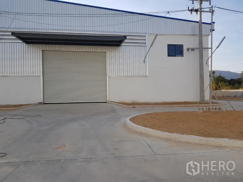 Factory for rent in Chon Buri - Modern factory exterior with large roller shutter door and concrete driveway.