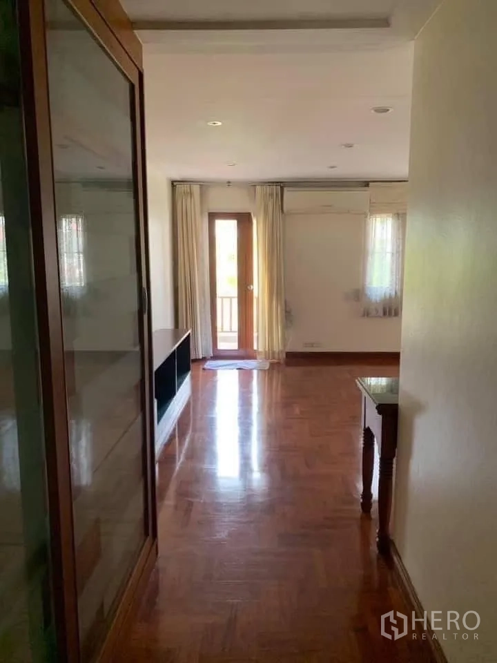 Townhouse for rent in Watthana, Bangkok - Corridor with polished wooden floor, glass cabinet and a door to a small balcony.