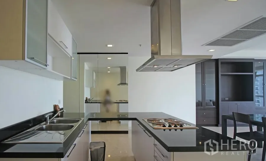 Condominium for rent in Khlong Toei, Bangkok - Modern U-shaped kitchen with black stone countertops, electric hob, range hood and double sink in an open-plan condo.