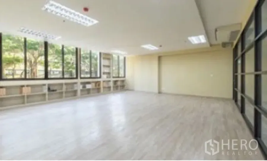 Office Space for rent in Chatuchak, Bangkok - Spacious office area with large windows, low built-in shelving, wood-look flooring, ceiling lights and glass partition.