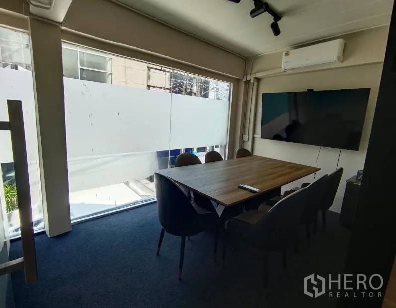 Shophouse for rent in Watthana, Bangkok - Glass-fronted meeting room with wooden table, six chairs and wall-mounted TV.