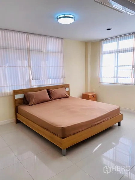 Detached House for rent in Watthana, Bangkok - Bright bedroom with wooden bed, large windows and glossy tiled flooring.