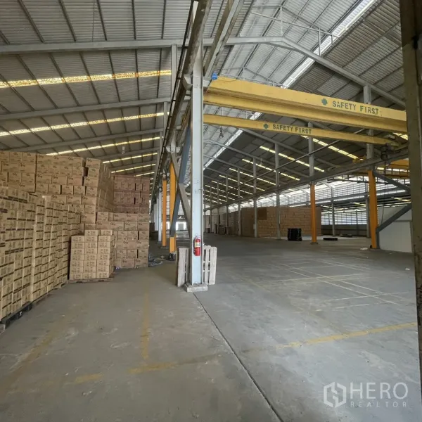 Factory for rent in Khlong Toei, Bangkok - Industrial aisle with overhead gantry cranes and stacked goods within the warehouse.
