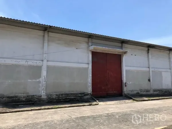 Warehouse for rent in Lat Krabang, Bangkok - Close-up of the warehouse facade featuring an oversized red loading door, concrete ramp and corrugated roof.