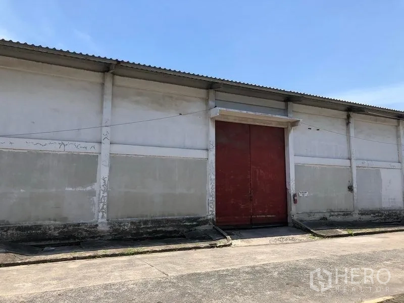 Warehouse for rent in Lat Krabang, Bangkok - Close-up of the warehouse facade featuring an oversized red loading door, concrete ramp and corrugated roof.